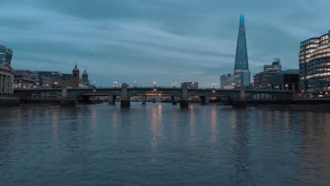 low drone shot along thames river under southwark bridge shard in background at sunset blue hour