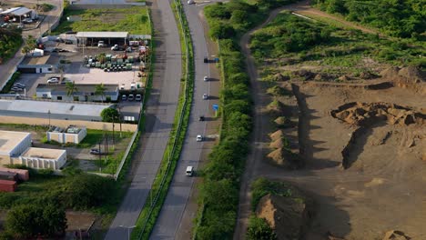 wide angle orbit above line of cars driving on highway with long shadows cast from greenery