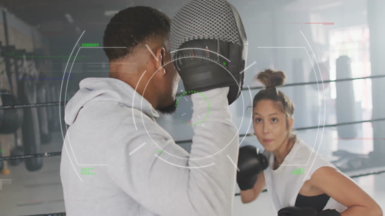 Male trainer holding mitts guiding female trainee boxing in ring displaying sports HUD graphics