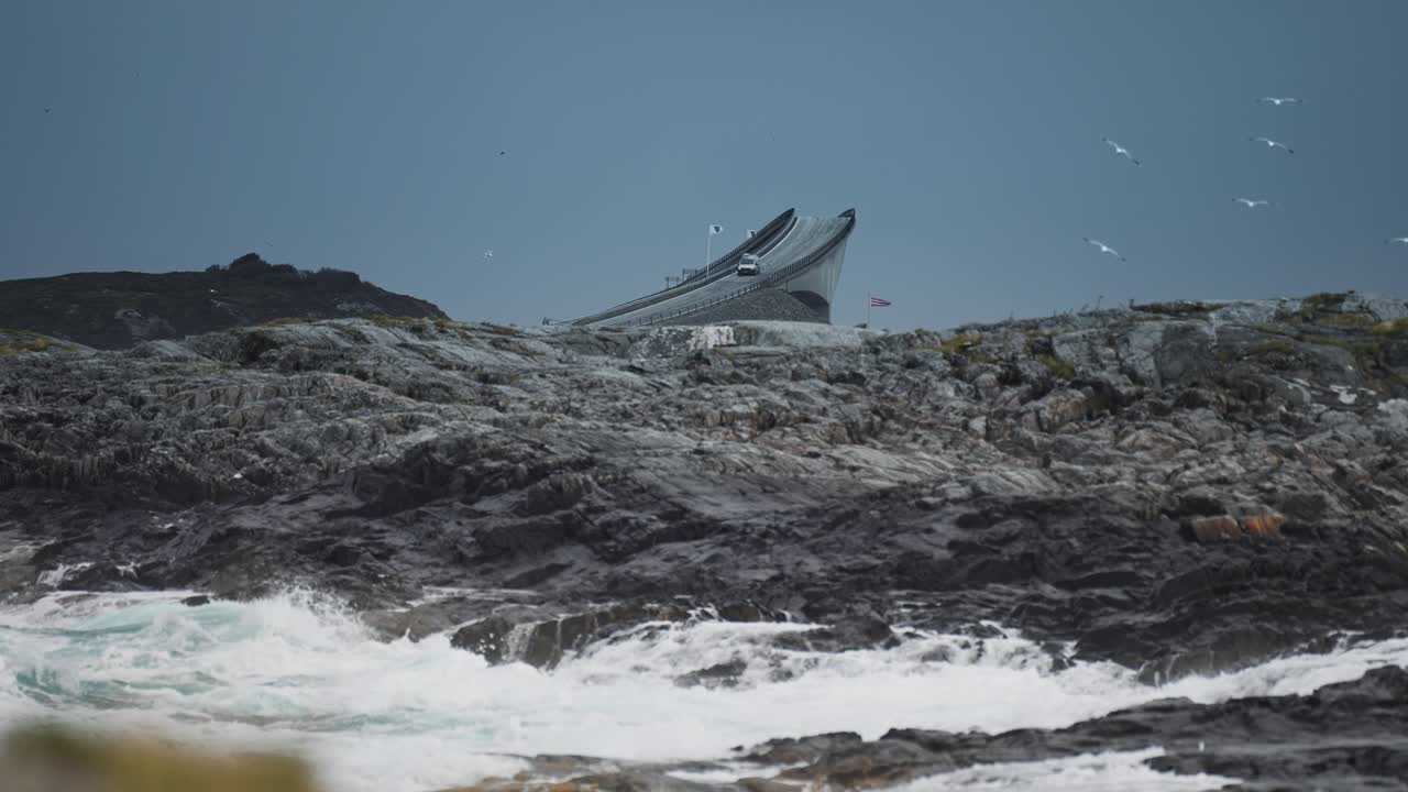 The iconic curve of Storseisundet Bridge rises against a backdrop of rocky coastline and crashing waves.