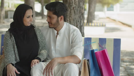 Front-view-of-happy-muslim-couple-sitting-on-bench-in-park.