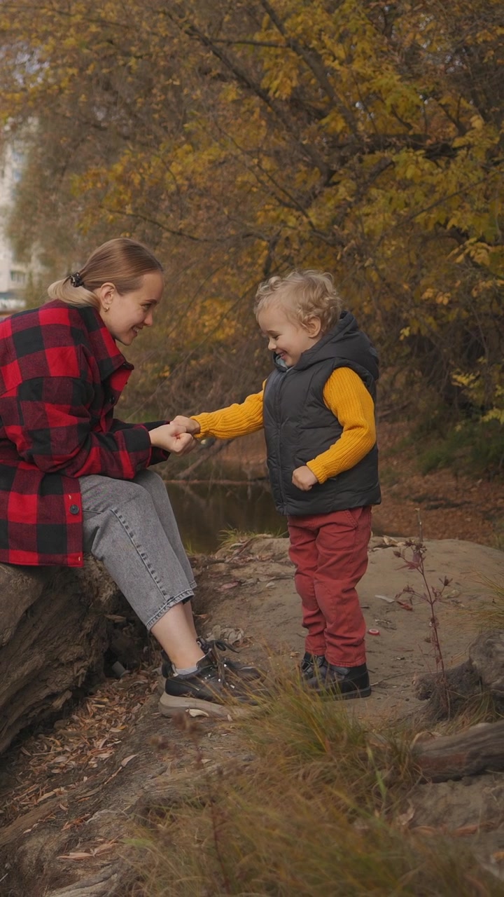 Madre e bambino piccolo che giocano insieme lungo un fiume in autunno
