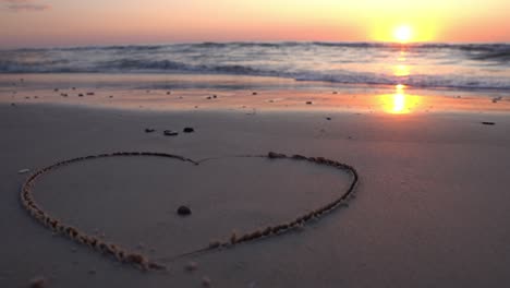 símbolo de corazón dibujado en la arena contra un telón de fondo de puesta de sol sobre el mar