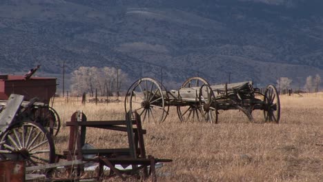 Una-Mirada-Panorámica-A-Los-Viejos-Vagones-Y-Otros-Equipos-Antiguos-Abandonados-En-La-Pradera-Con-Las-Montañas-Al-Fondo.