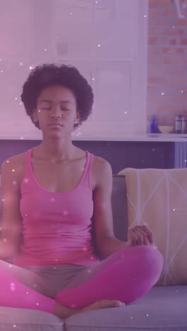 animation of light spots over african american woman practicing yoga and meditating at home