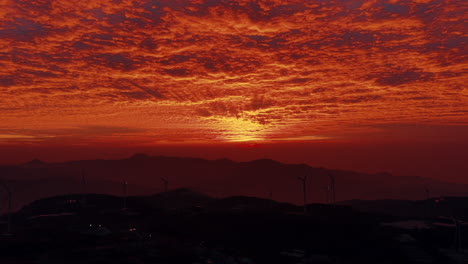fiery sunset over mountains with wind turbines