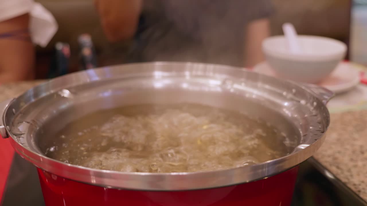 Åbning af en hotpot fyldt med boblende kogende suppe til en blandet grøntsags- og kødsuppe, på en restaurant i Bangkok, Thailand