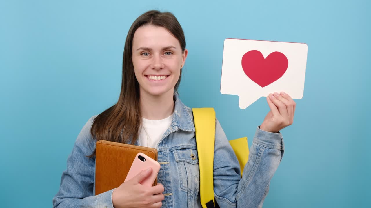 retrato de una chica bonita adolescente estudiante sostener libro, icono de reacción compartir repost comentario popular hacer clic, lleva mochila amarilla, aislado sobre la pared de fondo de color azul. educación, blogger, concepto en línea