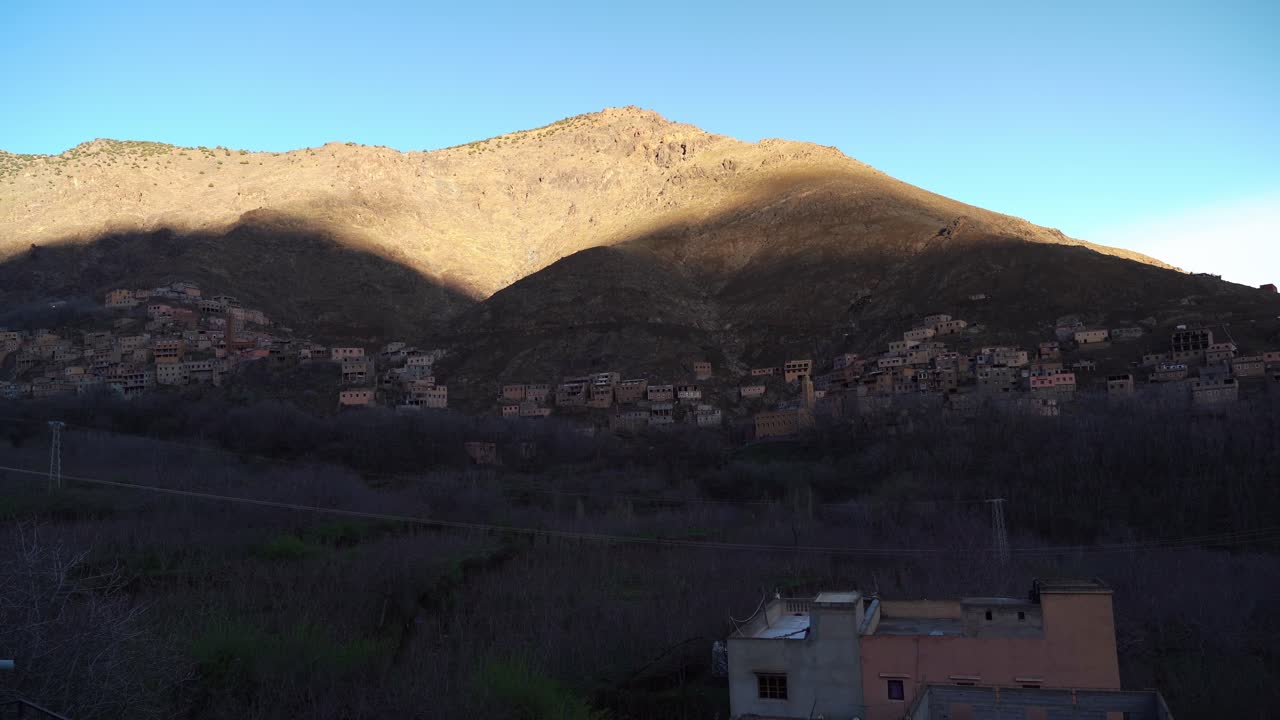 Shadows stretch across the terraced slopes of Imlil Village in Morocco, while the fading sunlight lingers on the highest mountain ridges