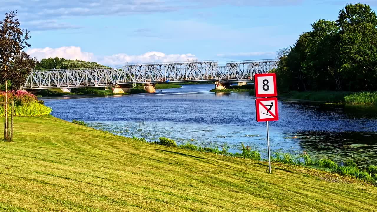 Railway Bridge Across River With "No Water Skiing" Sign and Calm Water Surface
