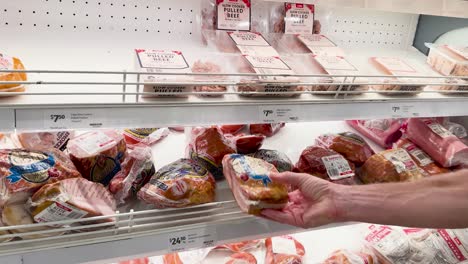 person choosing packaged meat from supermarket shelf