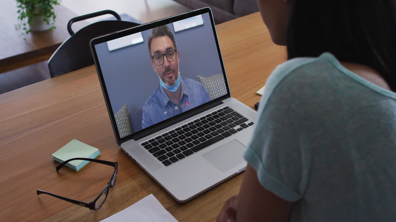 sección media de una mujer afroamericana haciendo una videollamada con un colega masculino en una computadora portátil