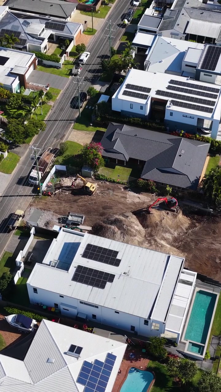 High-angle drone shot shows modern houses with solar panels near an active excavation site.