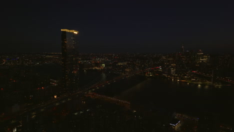 Aerial-panoramic-night-shot-of-One-Manhattan-Square-apartment-building-with-illuminated-rooftop-and-busy-road-on-Manhattan-bridge-to-Brooklyn.-Manhattan,-New-York-City,-USA