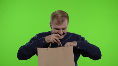 joyful man showing black friday inscription from shopping bags, smiling satisfied with low prices