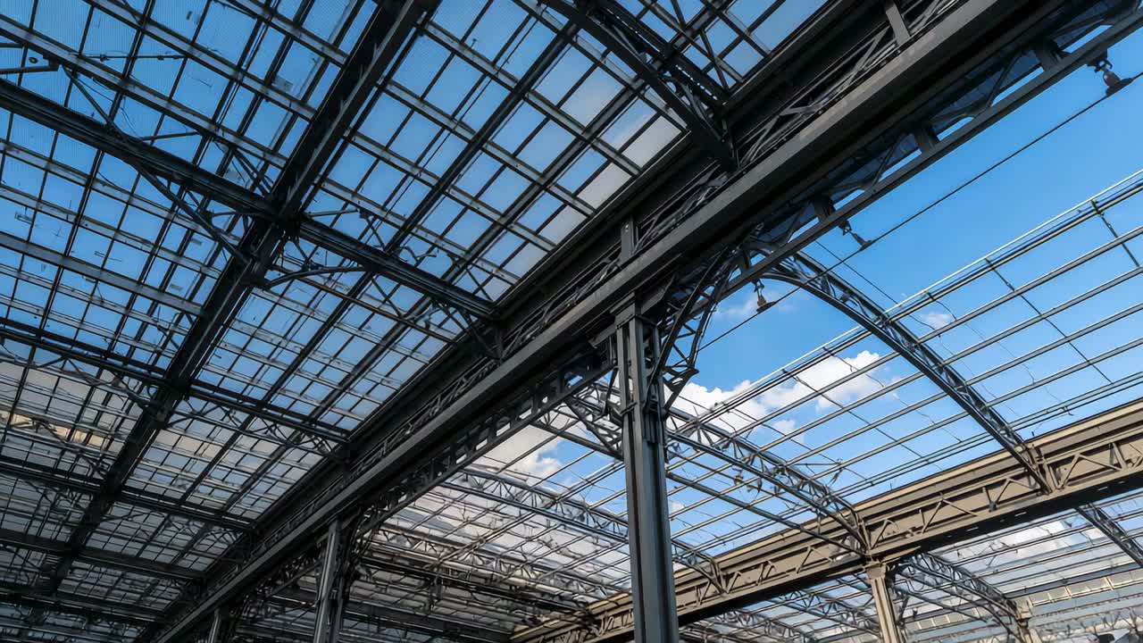 Panoramica della camera che inizia con una panoramica verso l'alto nell'atrio della stazione ferroviaria, rivelando pannelli di vetro e capriate ad arco in acciaio