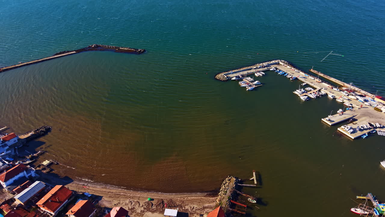 Lungomare con barche, piccoli edifici e acqua calma durante il giorno vicino a un porto