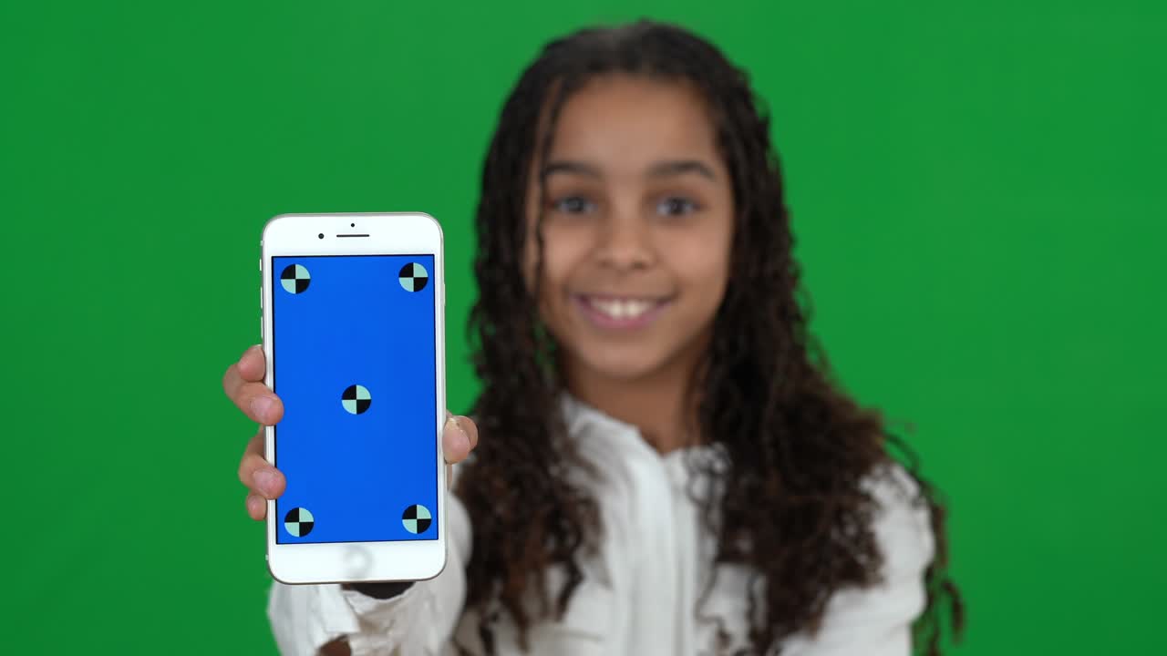 Close-up smartphone blue screen with African American teen girl smiling at chromakey background. Blurred happy teenager showing mobile app posing on green screen.