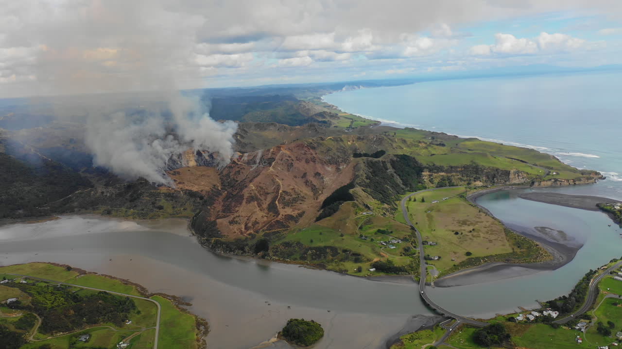Smoke from a brushfire rises against the scenic coastal landscape of New Zealand's North Island