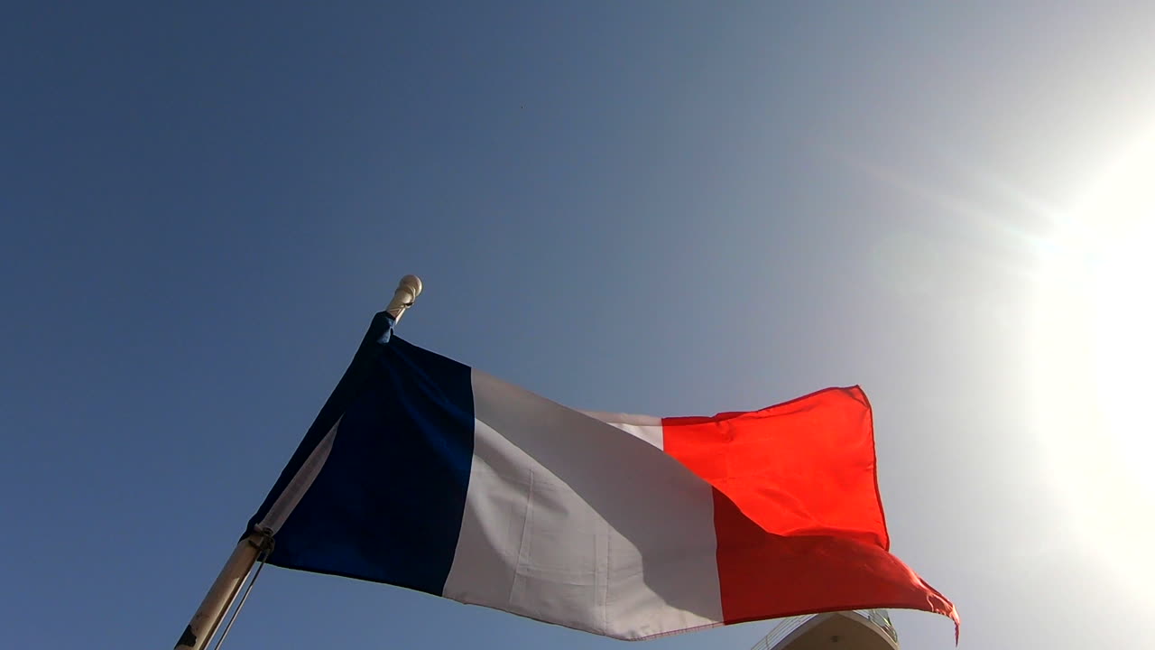 The french flag waving in slow motion on a bright sunny day with the blue sky and sun in the backround.