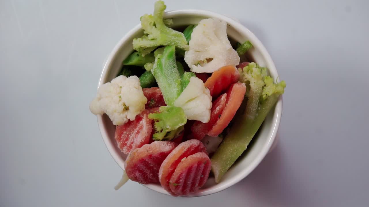 Bowl of colorful frozen vegetables on a white background