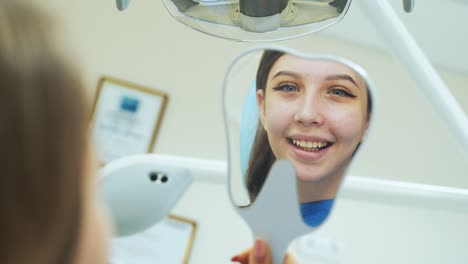 a young girl looks in the mirror in her hands as a dentist treats teeth in a clinic