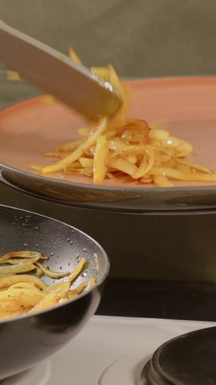 Vertical video: Hearing sizzle cook in green apron stirring in pan on stove, plating orange plate