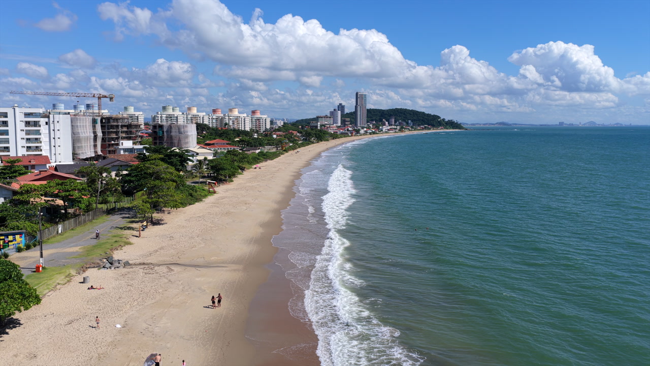 Drone view along Praia da Armação do Itapocorói, Penha, Santa Catarina, Brazil, showing sandy beach, coastal skyline, Atlantic Ocean and Ponta da Vigia headland.