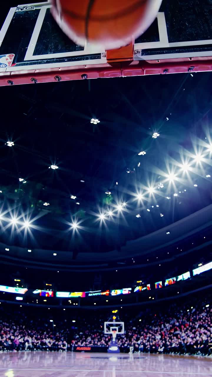 Dynamic low-angle shot of a basketball mid-air approaching the hoop in a stadium