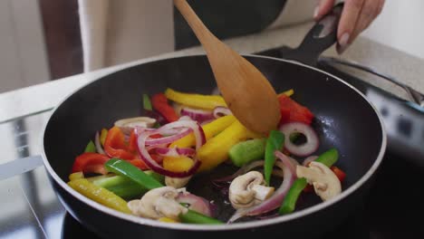 sección media de la mujer caucásica en casa en la cocina removiendo verduras en una sartén en la estufa con un