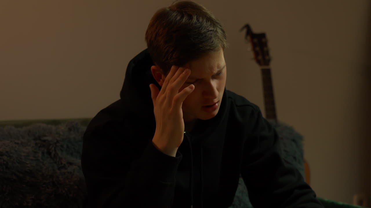 A guy having a headache while seated on a couch, massaging his temple, closeup