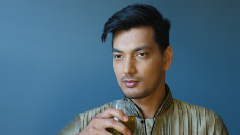 close-up view of indian young man in traditional clothes drinking hot tea and looking at camera