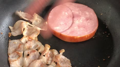 cocinando para el desayuno, freír el tocino y las piezas de tocino canadiense en una sartén. trozos crujientes de delicioso tocino se fríen en una sanduíche caliente. con ruido y fondo de bokeh enterrado.