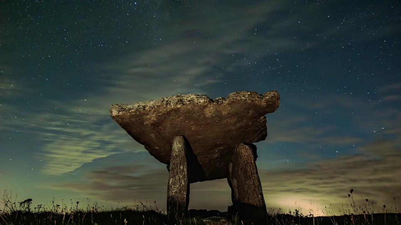 Noční časosběr Poulnabrone Dolmenu, The Burren, Irsko s Mléčnou dráhou a dramatickými mraky.