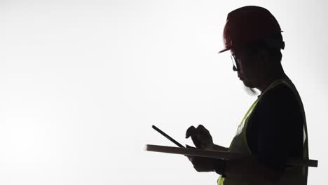 silhouette of an engineer with blueprints and tablet in hand working on a construction project