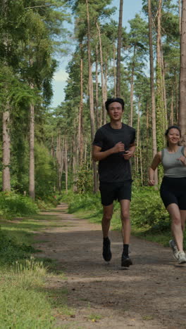 vertical video of couple exercising doing work out outdoors running along track through forest towards camera wearing sports clothing shot in real time 3