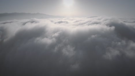 rising aerial footage above thick cloud cover over mountain peaks