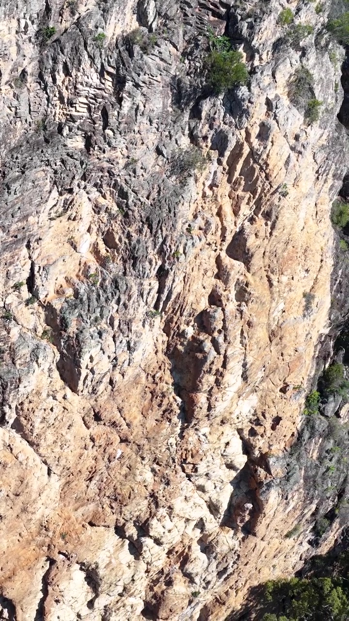 Un filmato aereo cattura aspre formazioni rocciose a Nimbin, NSW, sotto la luce intensa del giorno, evidenziando texture naturali e tonalità terrose.