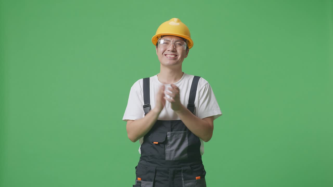 Asian Man Worker Wearing Goggles And Safety Helmet Smiling And Clapping His Hands While Standing In The Green Screen Background Studio