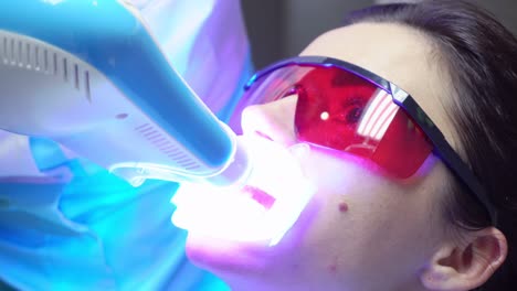 young woman with an expander in mouth and red protective glasses getting uv whitening at the dentist's office by an ultra violet machine. shot in 4k