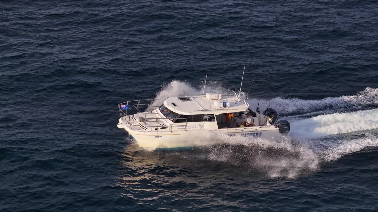 A commercial fishing charter boat speeds across open ocean waters off the Gold Coast, Australia, captured in golden sunset light with smooth aerial camera movement