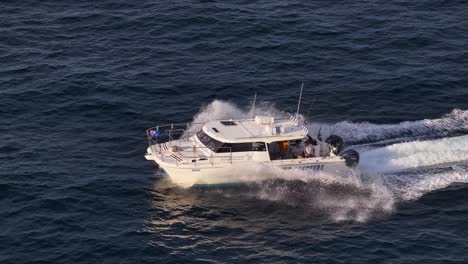 a commercial fishing charter boat speeds across open ocean waters off the gold coast, australia, captured in golden sunset light with smooth aerial camera movement
