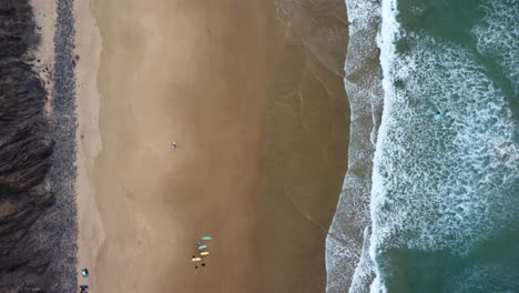 drone shot of the coast with surfers in arrifana beach, portugal