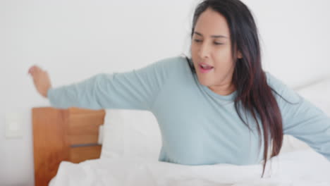 Stretching in bed, asian woman waking up and smiling, starting her day relaxed, at home