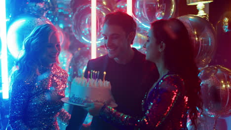 happy friends congratulating guy in nightclub. man blowing candles at party