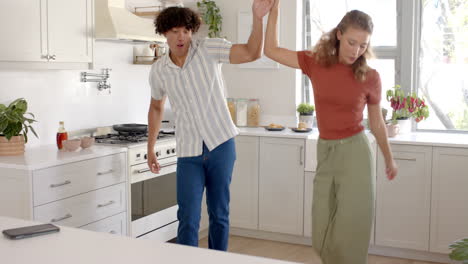 diverse couple laughing together while looking at smartphone in modern kitchen, at home