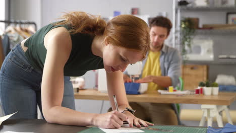 diseñadora de moda dibujando diseño en primer plano mientras su colega trabaja en la máquina de coser