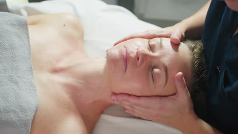 high angle view of beauty expert massaging client head and neck while client closes her eyes softly on massage chair in spa with white background during tranquil therapy session showcasing hands