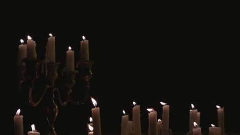 a group of white candles some on a candelabra lit up and running for a while