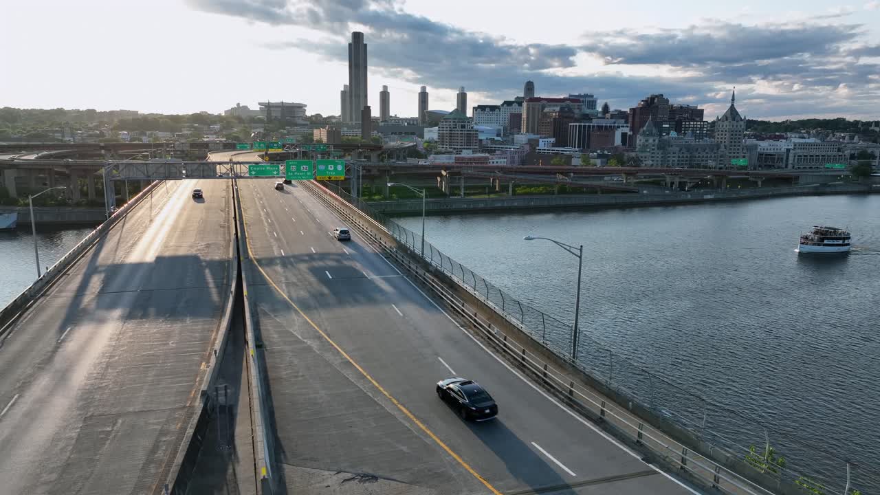 Cars on Bridge and cruising ship on Hudson River at sunset. Aerial rising wide shot. Albany city skyline in New York, America. Summer evening in USA